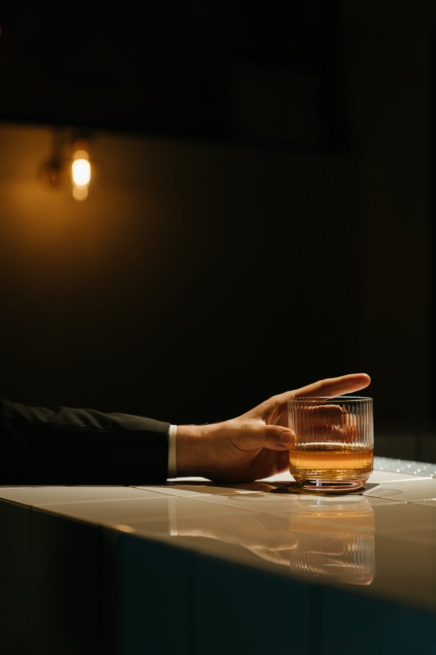 person pouring brown liquid on clear drinking glass